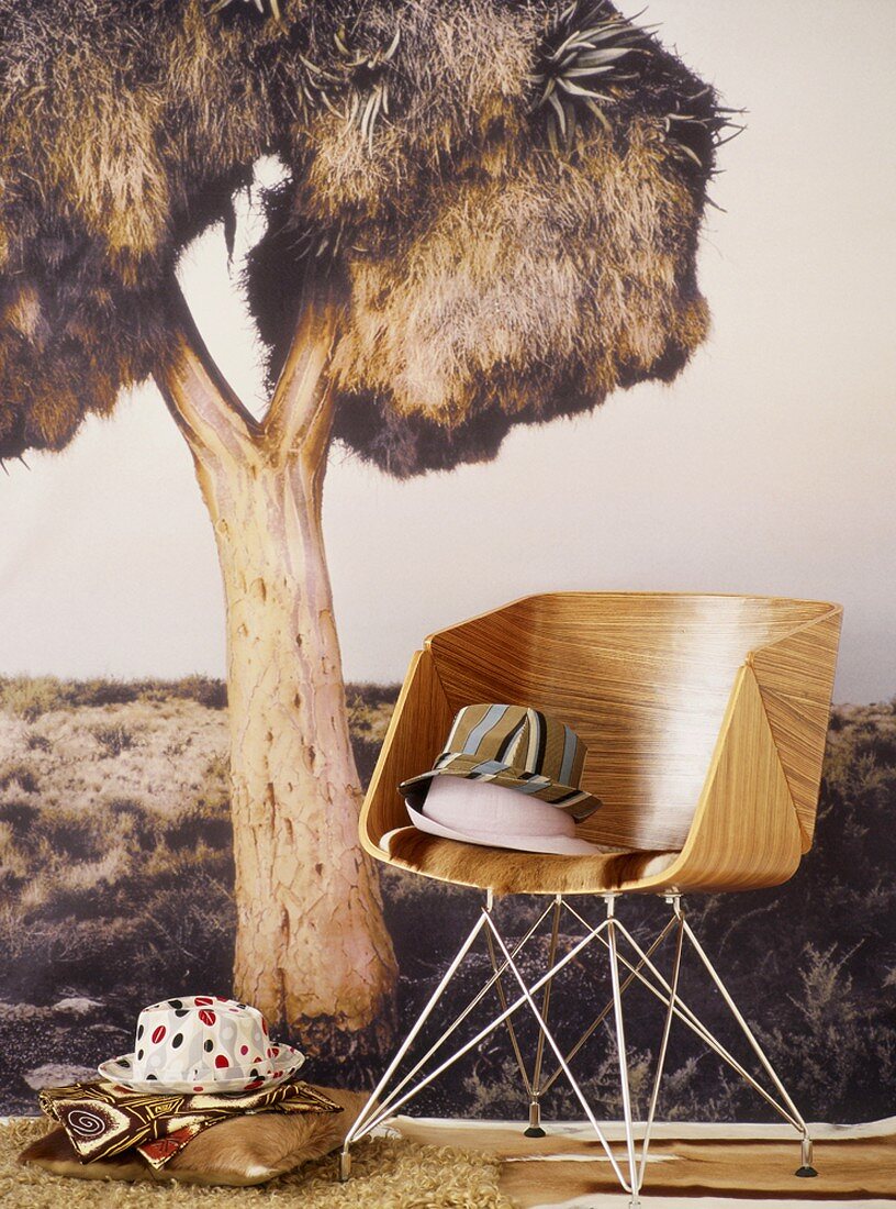 Holzstuhl mit Stoffhüten vor einer Fototapete mit exotischem Baum
