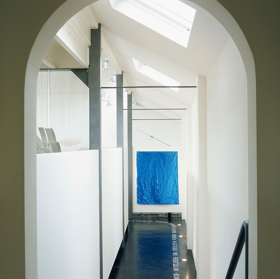Corridor with blue artwork and strip of lettering on dark floor next to half-height partitions
