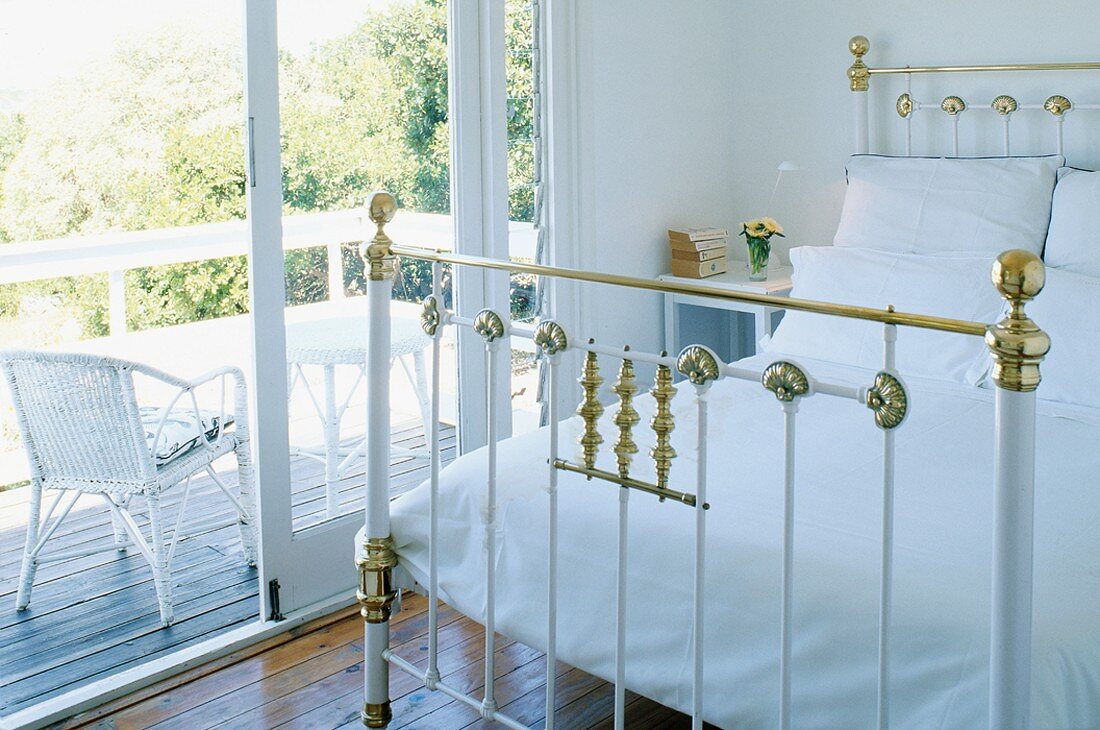 Metal bed frame with brass ornaments and view of white wicker chair through open terrace door