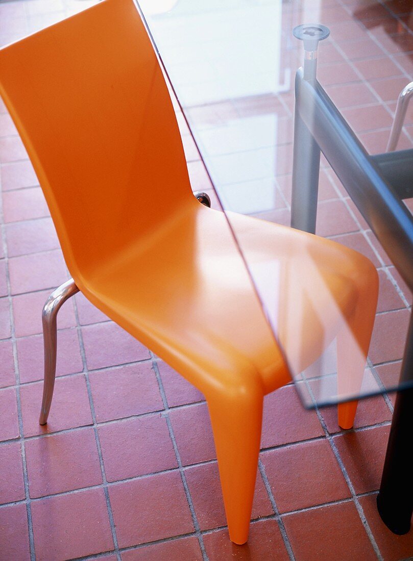 Orangefarbener Kunststoffstuhl und moderner Glastisch auf Terracottafliesen
