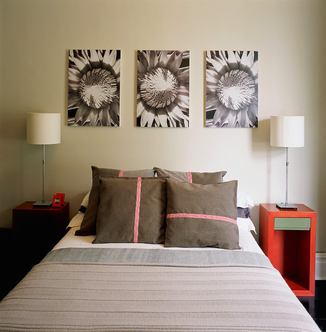 Doppelbett mit Zierkissen, flankiert von roten Nachtkästchen mit Tischlampen und Schwarzweiss-Fotos mit Blütendetails