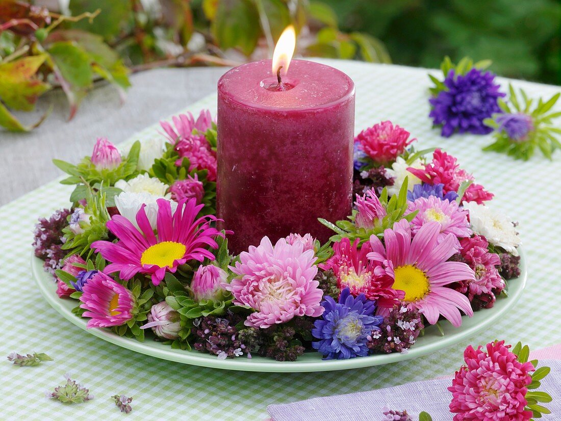 Candle in wreath of asters and oregano on plate