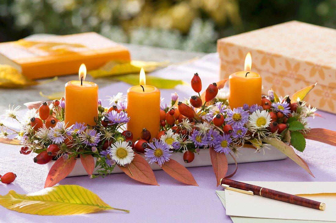 Herbstgesteck mit Blumen, Hagebutten und Kerzen auf Tisch