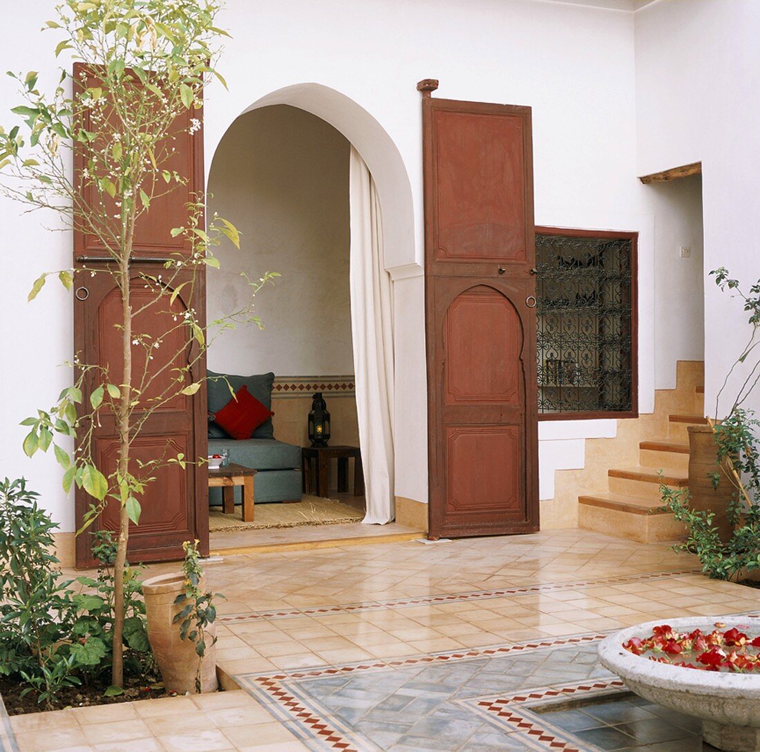 Tiled, Oriental-style courtyard with fountain basin and view through wooden door into seating area with side tables