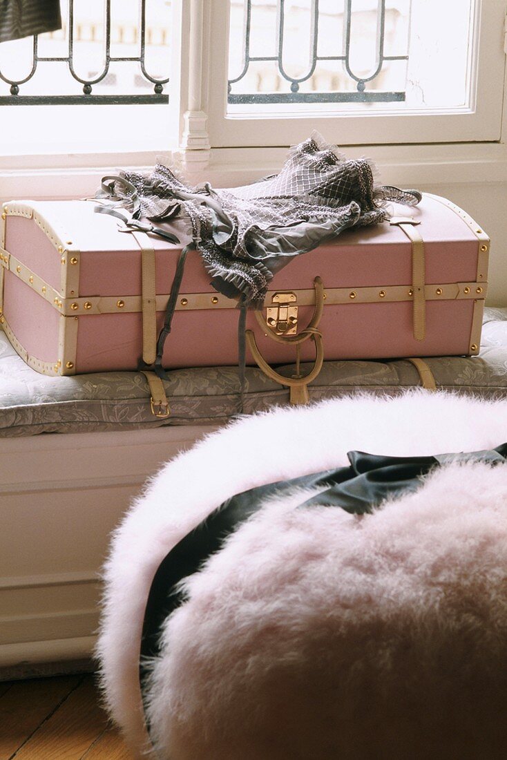 Lingerie on pink vintage suitcase and bundle of faux fur with black ribbon