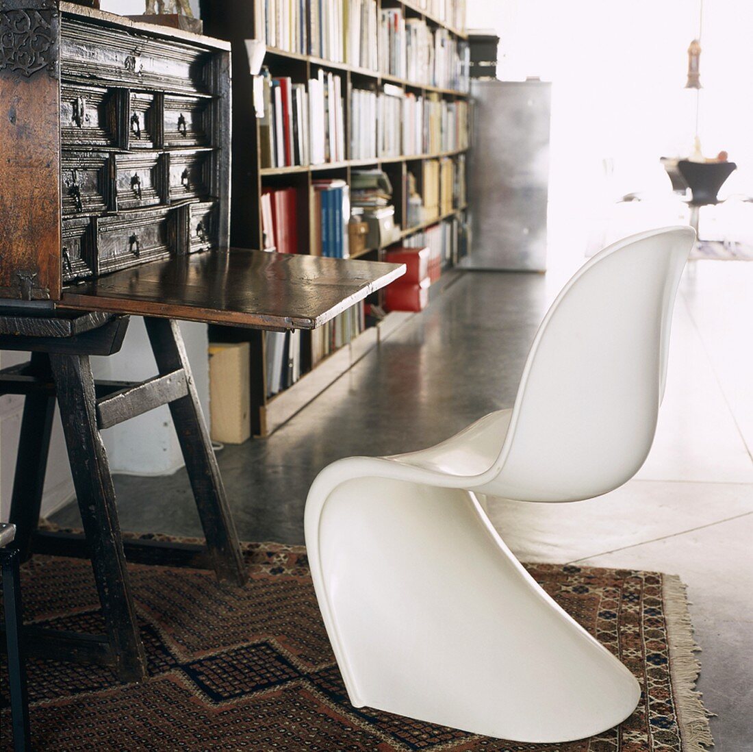 Weisser 60er Jahre Kunststoff-Schalenstuhl vor einem antiken Sekretär und Bücherregalen im Hintergrund