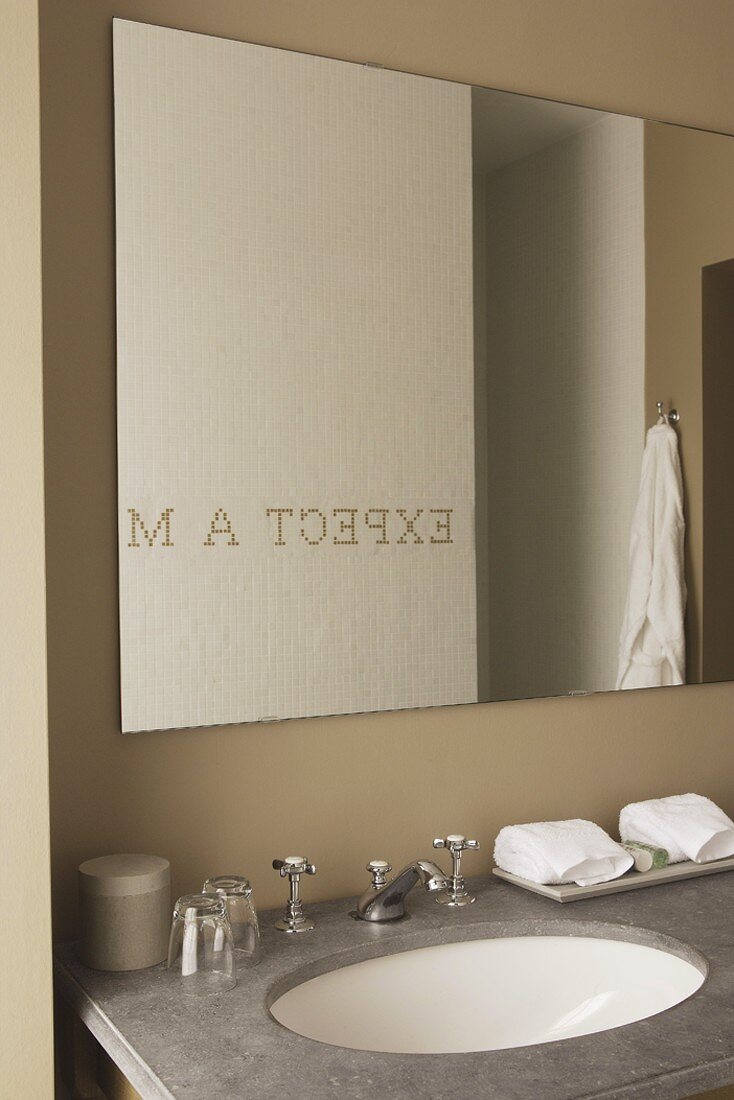 Spiegelung eines Schriftzuges im Badezimmerspiegel über einem Marmorwaschtisch mit Retro-Armatur