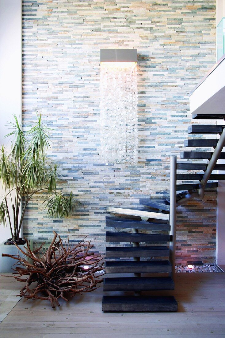 Wandleuchte mit Kristallvorhang an Natursteinwand und gewendelte Treppe auf eine Wohnraumgalerie