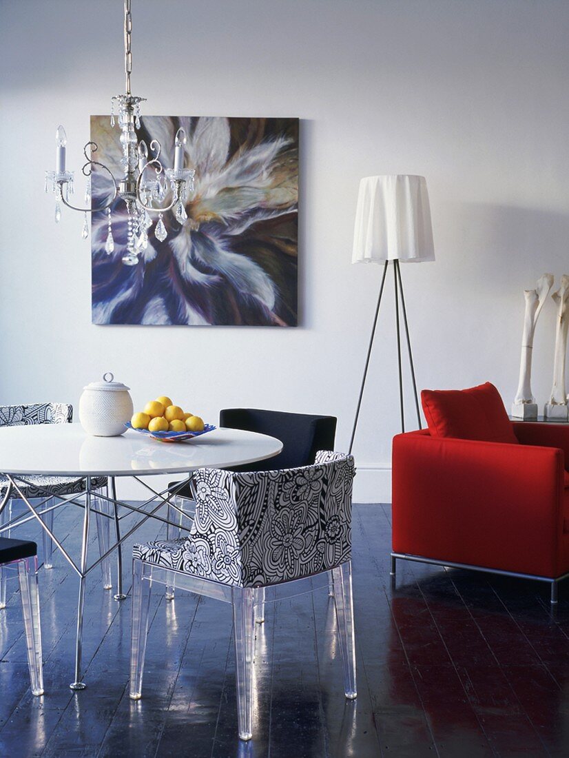 Orgineller Stilmix im Wohnraum - Designer Stühle mit Plexiglas-Beinen um einen runden Tisch und Dreibein-Stehlampe