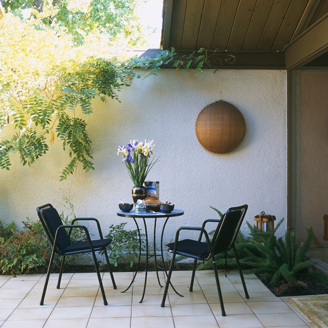 Terrasse mit rundem Tisch und Stühle vor weisser Wand
