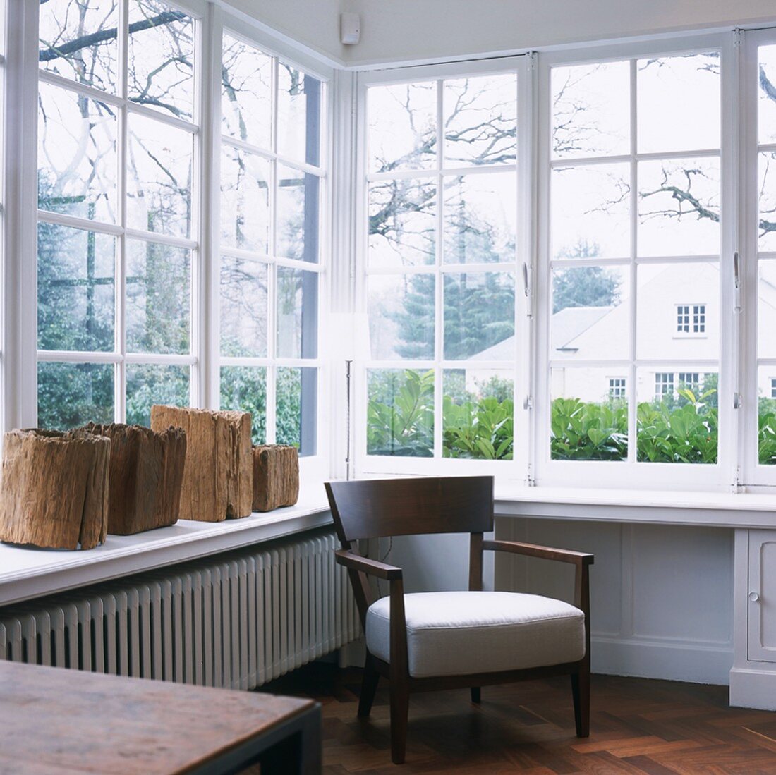 Wintergarten mit Polsterstuhl am Fenster und rustikalen Holzstücken