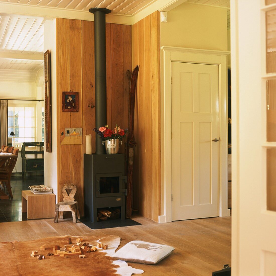 Holzverkleideter Wohnraum mit Kaminofen in einer Ecke und Tierfell als Teppich