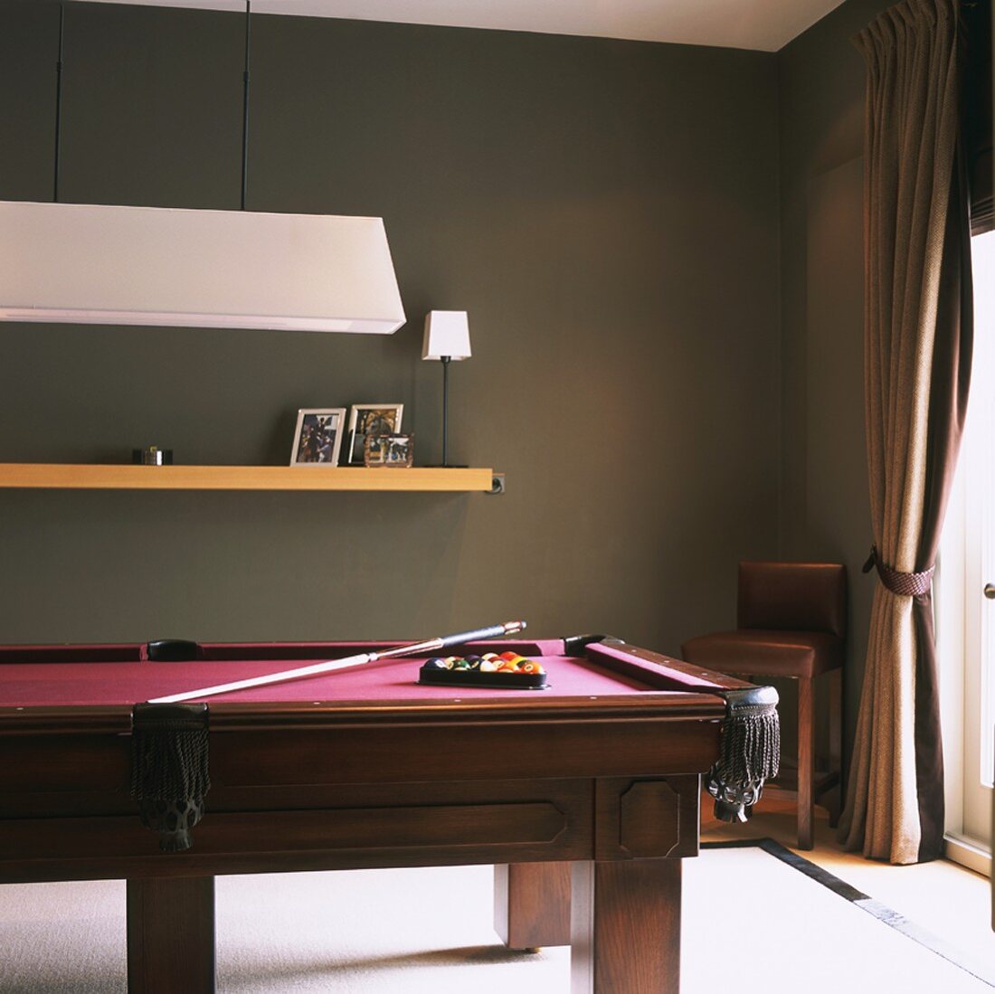 Corner of room with heavy pool table, wooden floating shelf and French doors with curtain