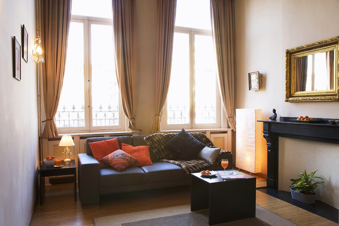 Helles Wohnzimmer mit schwarzer Ledercouch und Spiegel mit Goldrahmen über ehemaligem offenen Kamin