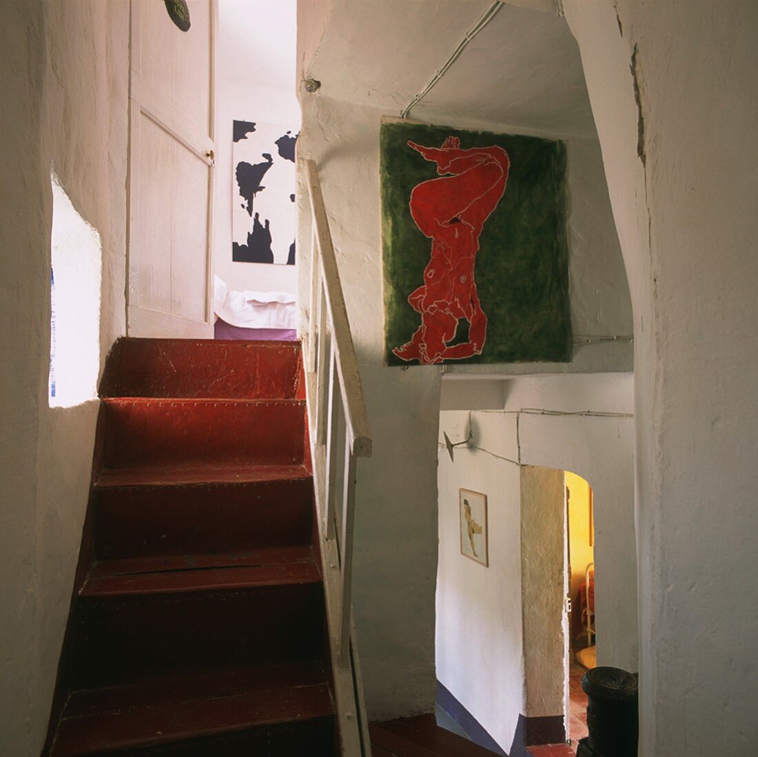 Stairwell with red staircase, white wooden balustrade and modern paintings on wall