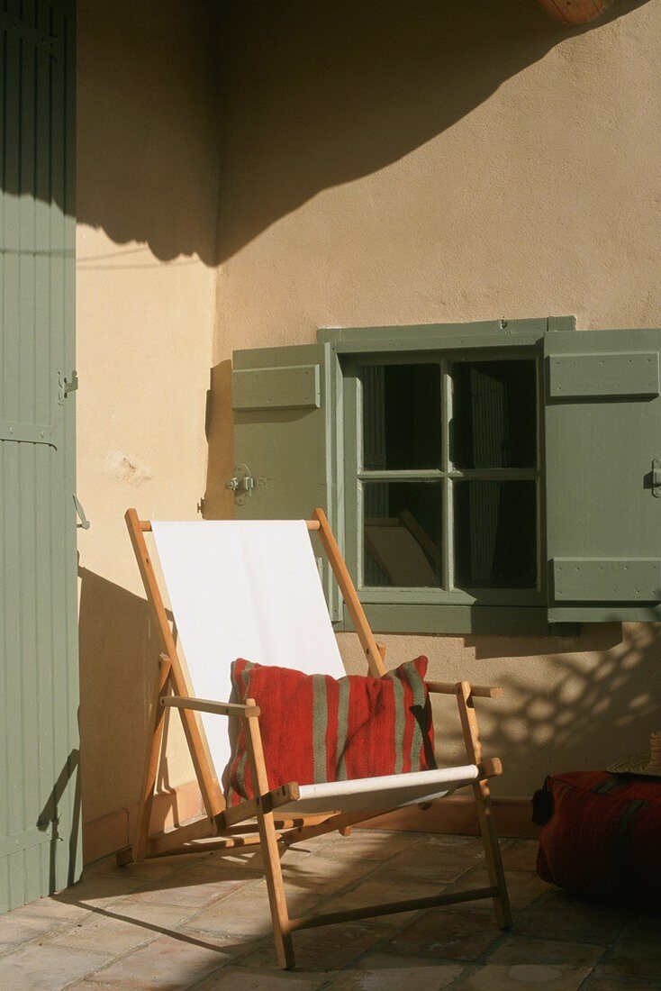 Sonnenbeschienener, kleiner Innenhof mit weißem Liegestuhl und Ethnokissen