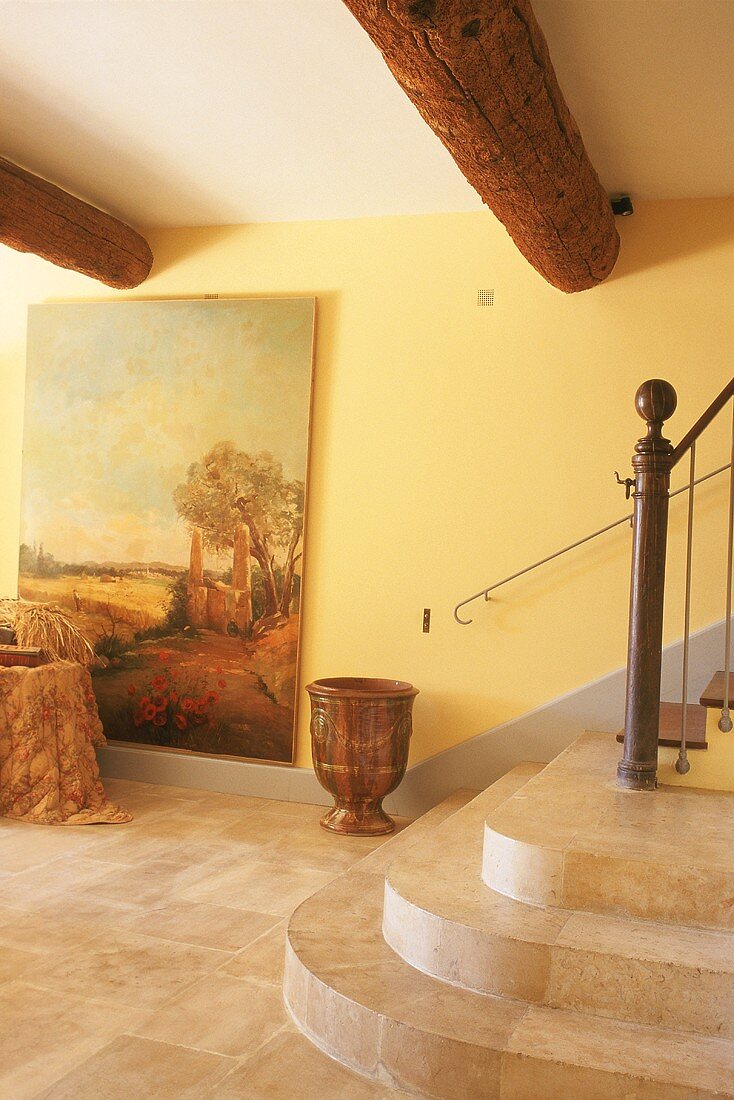 Treppenraum mit Steinfliesen, Steinstufen, größem Ölgemälde an der Wand und rustikalen, runden Holzbalken an der Decke
