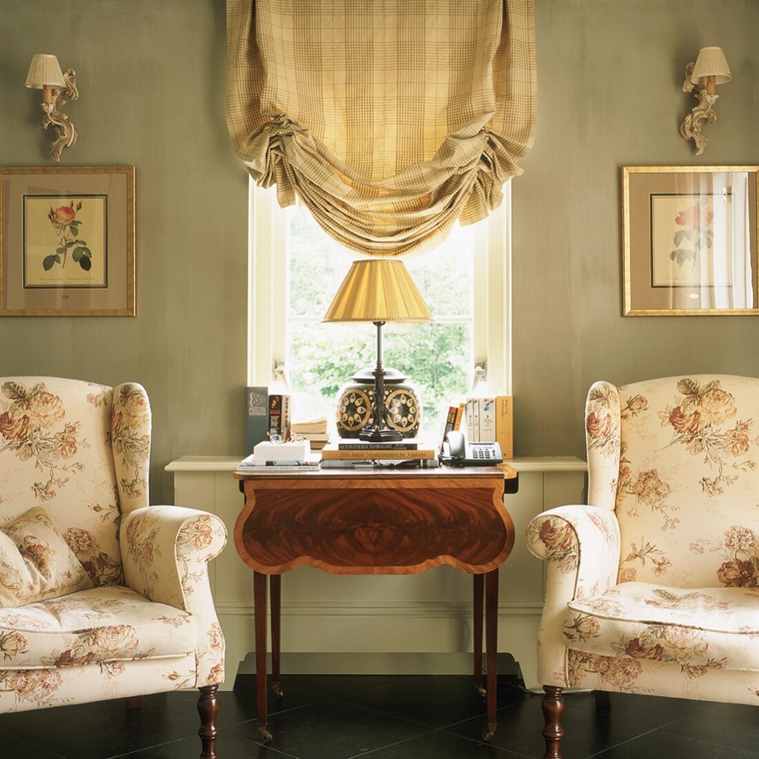 Elegante Sessel mit floralem Muster; dazwischen ein antiker Beistelltisch unter einem Fenster mit kariertem Raffrollo