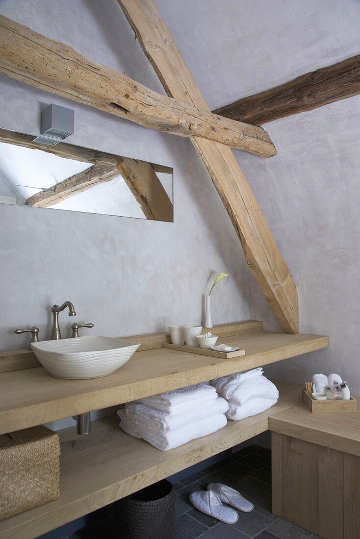 Washstand made from thick wooden boards and long narrow mirror under sloping attic ceiling with exposed beams