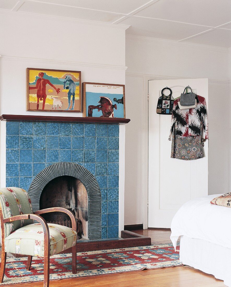 Offener, blau gekachelter Kamin in Schlafzimmer mit Teppichläufer, Sessel und modernen Bildern an der Wand