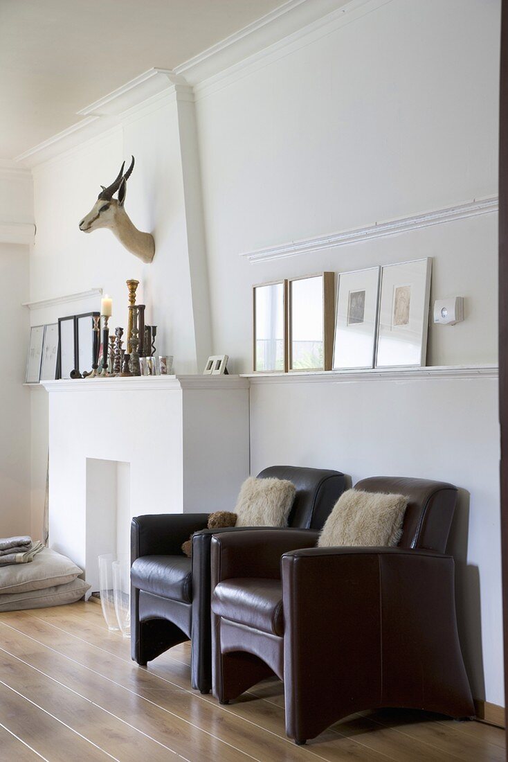 Two leather armchairs with fur cushions next to fireplace, hunting trophies and floor cushions