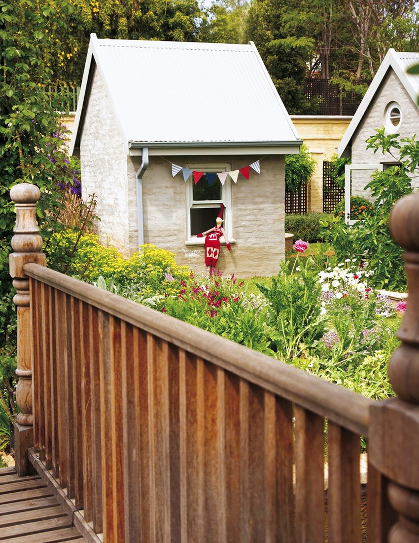 Dekoriertes Gartenhäuschen mit bunten Wimpeln hinter Gartenblumen und Holzbrücke