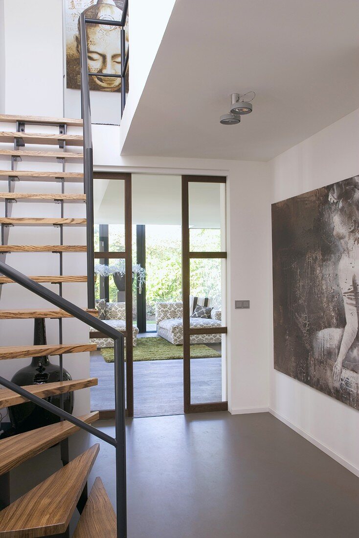 Treppenraum mit Holztreppe und Blick in den Wohnraum durch eine gläserne Schiebetür