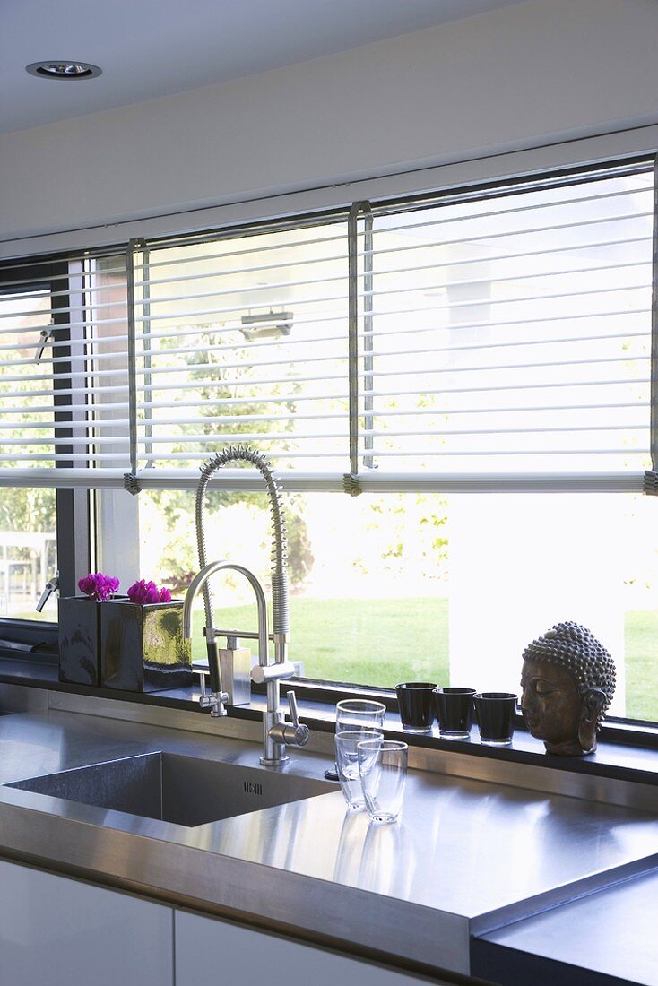 Kitchen counter with stainless steel sink and louver blinds on long windows