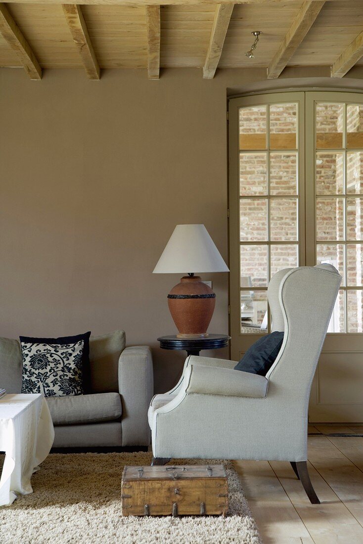 White wing-back chair in living room with wood-beamed ceiling