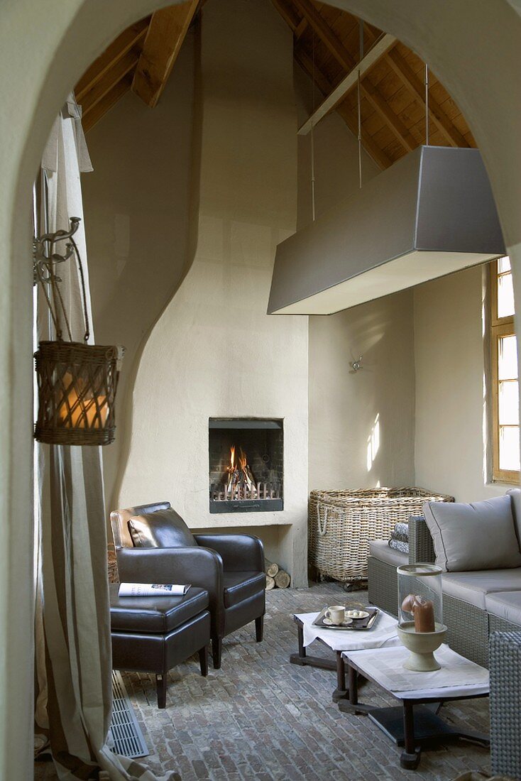 Rustic room with exposed roof beams, open fireplace, brick floor, elegant seating and large basket in corner