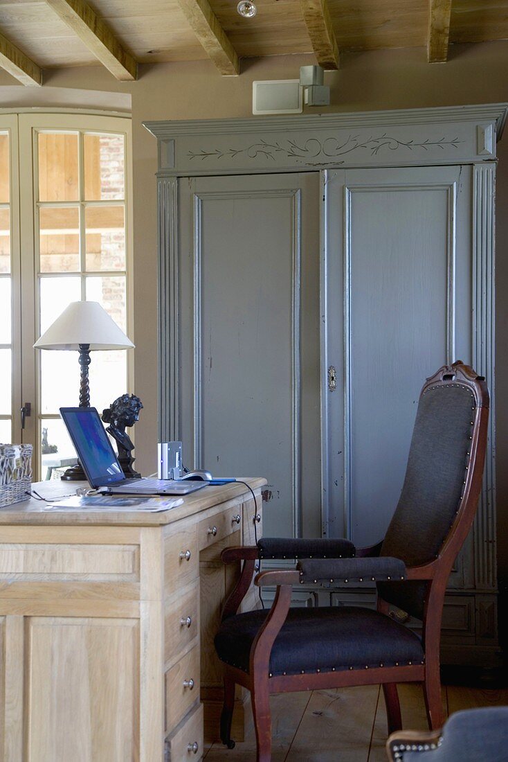Arbeitsplatz mit einfachem Schreibtisch aus Holz, einem gepolsterten Stuhl und einem blauen Holzschrank im Vintagelook