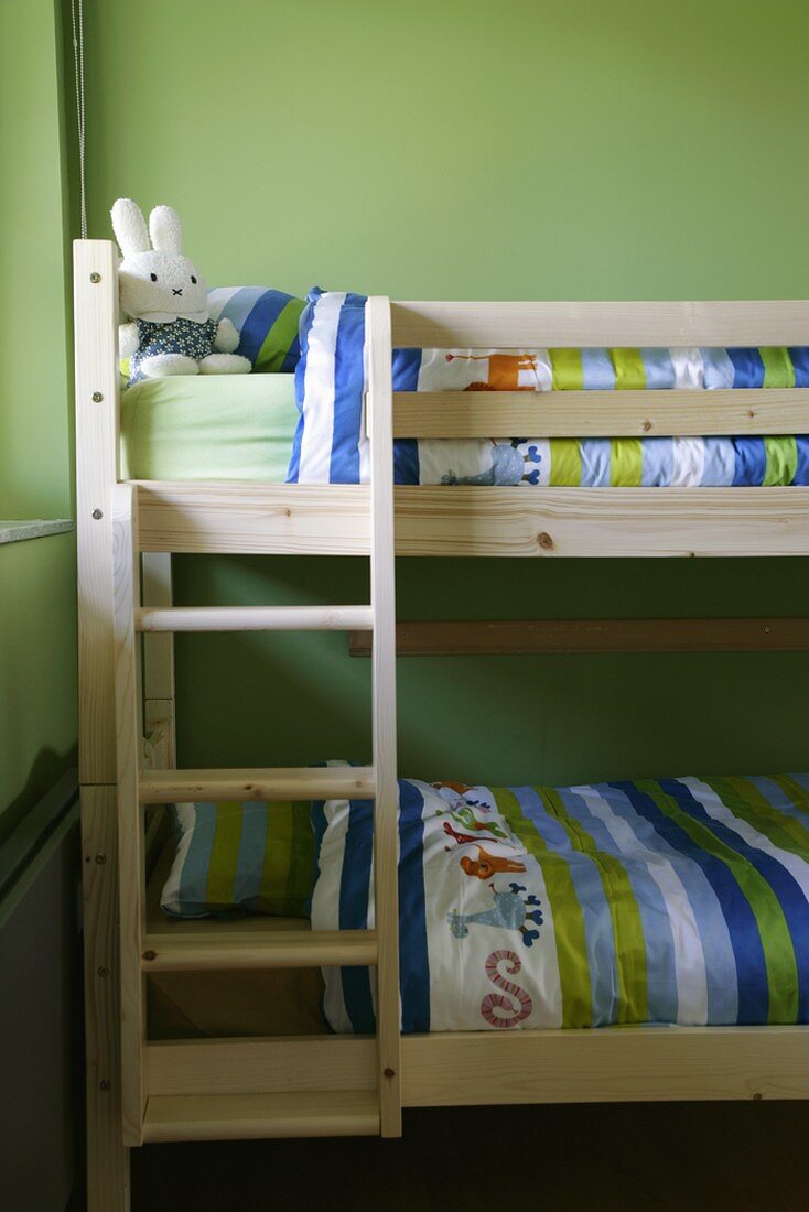 Einfaches Holz-Etagenbett mit farbenfroher Bettwäsche und lustigem Stoffhasen im Kinderzimmer