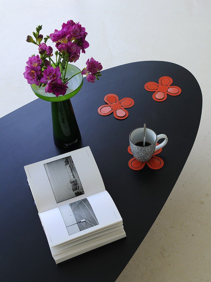 Book, cup of coffee and vase of flowers on designer table