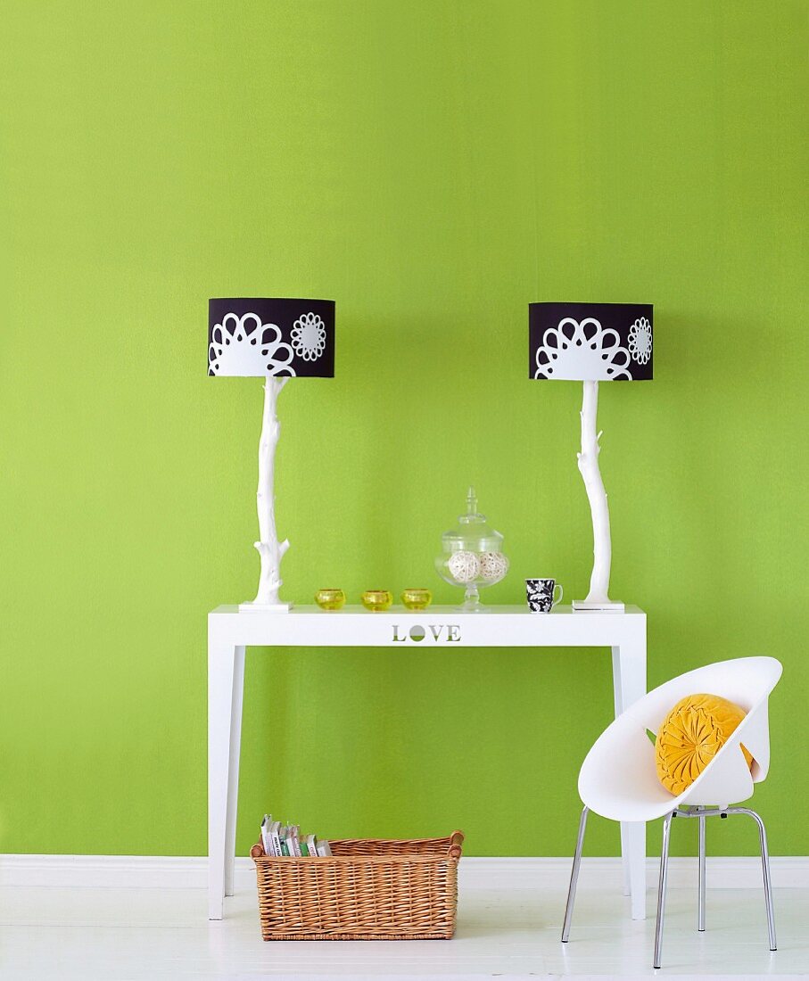 Two table lamps with black and white lampshades on table and child's chair in front of green-painted wall