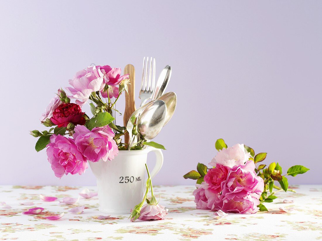 Cutlery and roses in a measuring jug