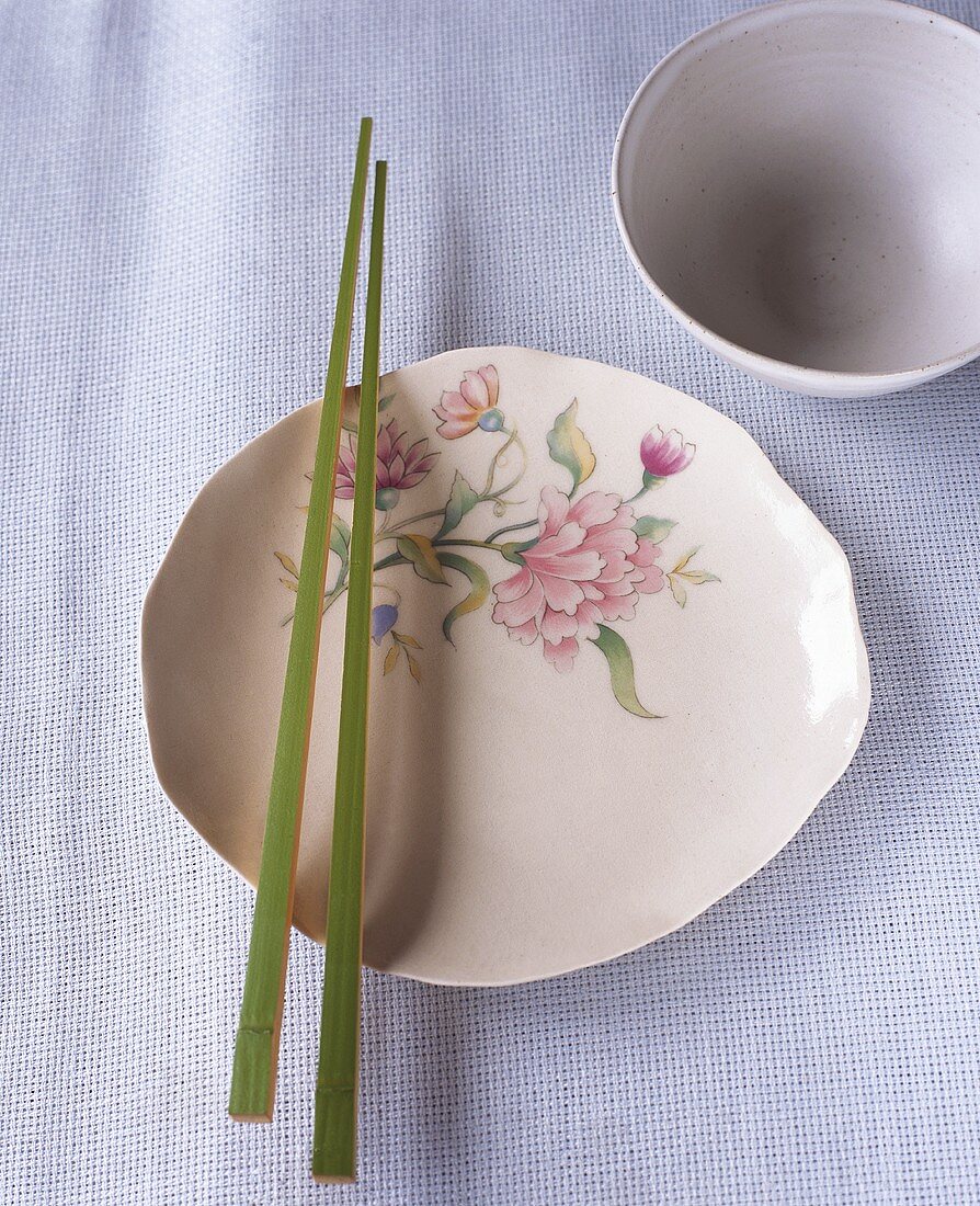 Teller mit Blumendeko, Essstäbchen und Reisschale