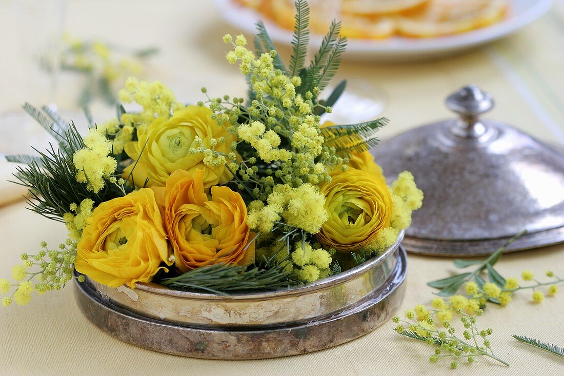 Arrangement of ranunculus and mimosa in a silver dish