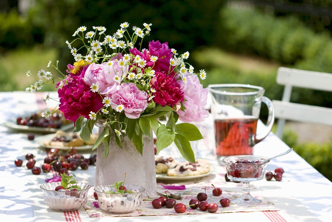 Tisch im Garten mit Kirschdesserts und Blumenstrauss