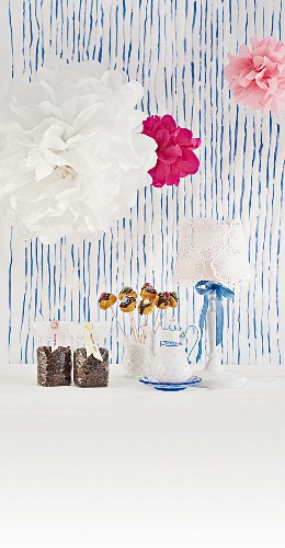 Ideen für den Kaffeetisch - Deko Pompons, Tischlampe mit Tortenspitzen, Cake Pops und verpackte Kaffeebohnen vor blauem Streifenmuster