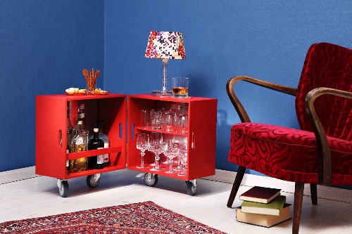 DIY minibar made from two wooden crates on castors covered in wallpaper next to 50s armchair