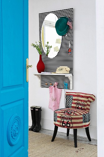 View past bright blue interior door to DIY cloakroom panel with hat pegs, mirror and shelf on black-and-white-striped back