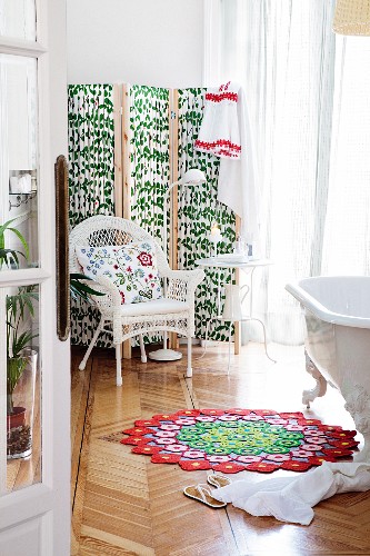 DIY Badewannenvorleger aus Häkelblüten, Korbstuhl mit floralem Kissen und Paravent mit Blättermuster im Hintergrund