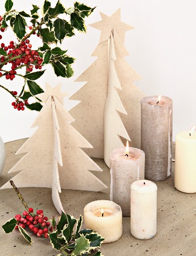 Selbst gebastelte Weihnachtsbäume aus Filz und brennende Kerzen auf Betontisch mit Stechpalmenzweigen