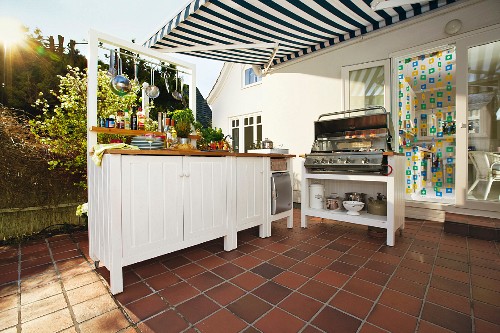 White-painted base units on tiled summer terrace with DIY outdoor kitchen