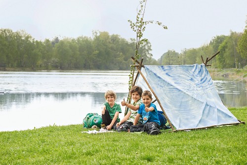 Children in tent made from branches and sheet on river bank