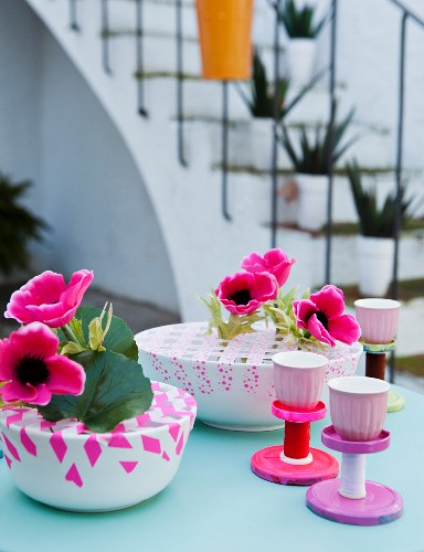 Colourful table decorations: bowls of anemones criss-crossed with washi tape and stands hand-made from jar lids and thread reels