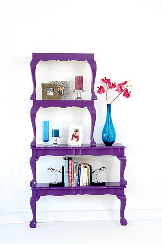 Books and blue glass vases on antique-style tables halved, painted purple and stacked to make decorative shelves