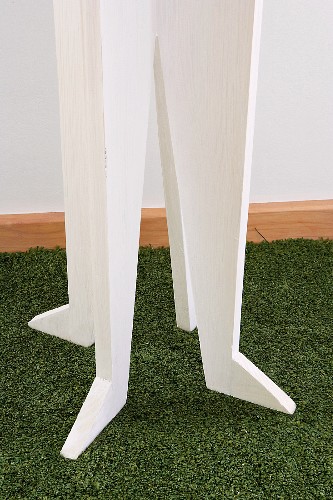 Detail of white-painted, wooden coat rack on green, artificial lawn rug