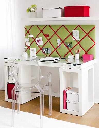 Designer plexiglass chair at modern desk with upholstered panel on wall below shelf