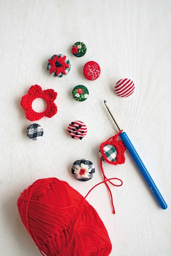 Embroidered buttons with crocheted flower motifs, crochet hook and ball of red wool